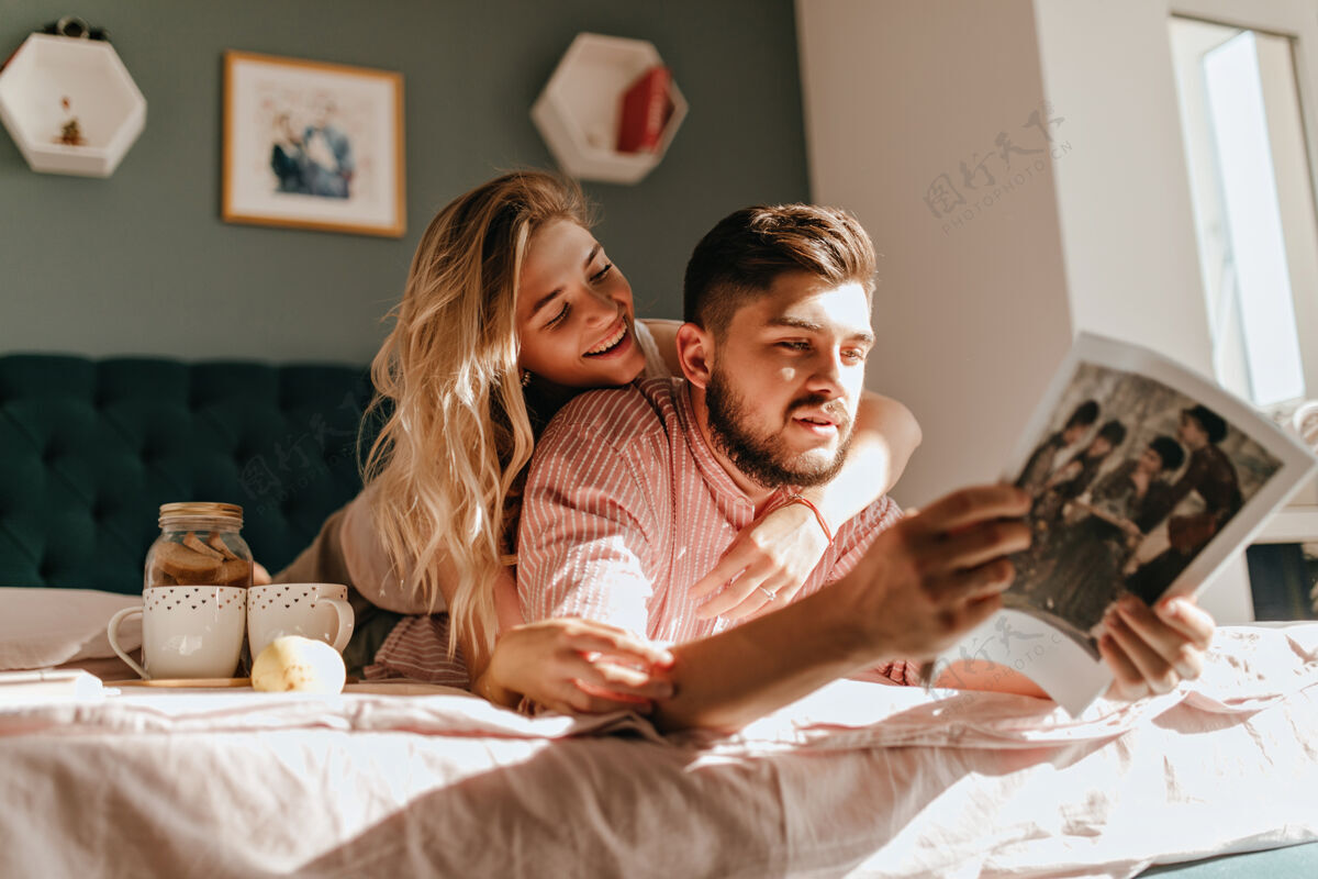 约会夫妻俩躺在床上 一边喝着曲奇饼喝着早茶拥抱着的男人和女人正在看时尚杂志关系早餐宠物