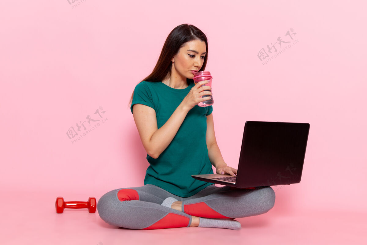 女性正面图穿着绿色t恤的年轻女性在粉色墙壁上使用笔记本电脑腰部运动锻炼美丽苗条运动员运动员减肥工作