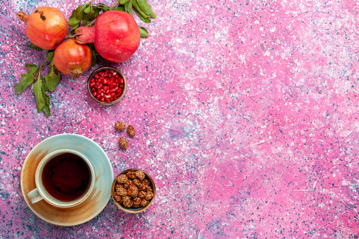 咖啡顶视图新鲜石榴与绿叶和一杯茶在粉红色的表面新鲜树生的
