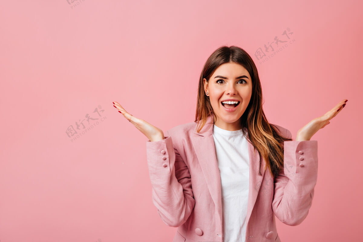 大笑兴奋的高加索女士举起手站着摄影棚拍摄的粉红色背景上孤立的漂亮黑发女人时尚优雅自信
