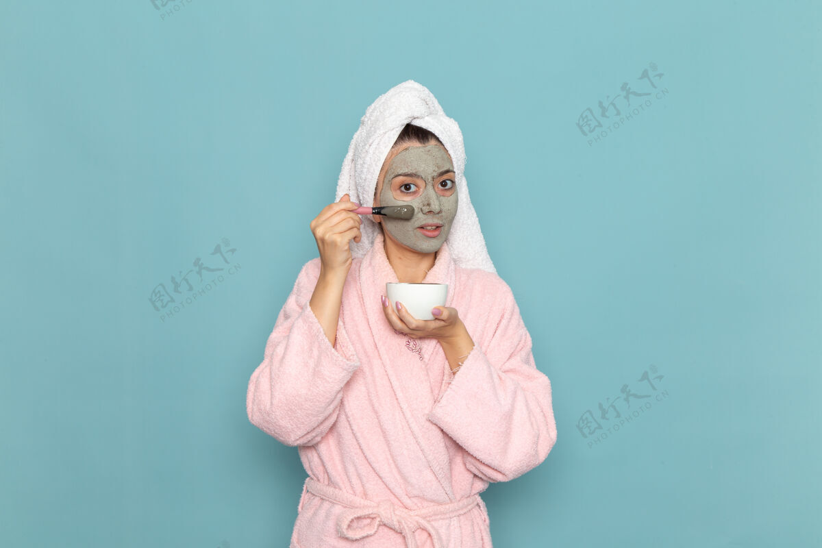 尺子正面图年轻女性穿着粉色浴袍淋浴后在蓝色墙壁上涂抹护肤霜美容水自我护理淋浴干净自我护理年轻人女性