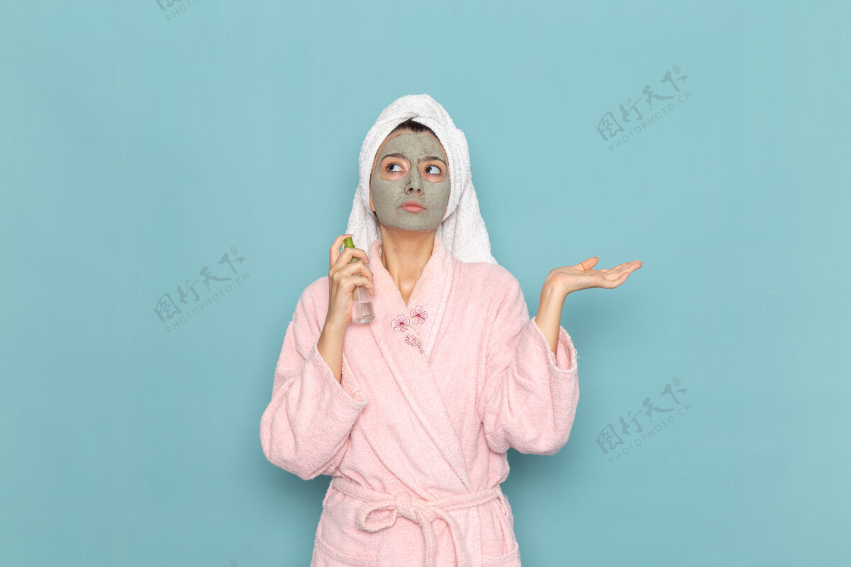 清洁正面图身着粉色浴袍的年轻女性淋浴后手持喷雾在蓝色墙面上清洗美容净水自护霜淋浴后年轻淋浴