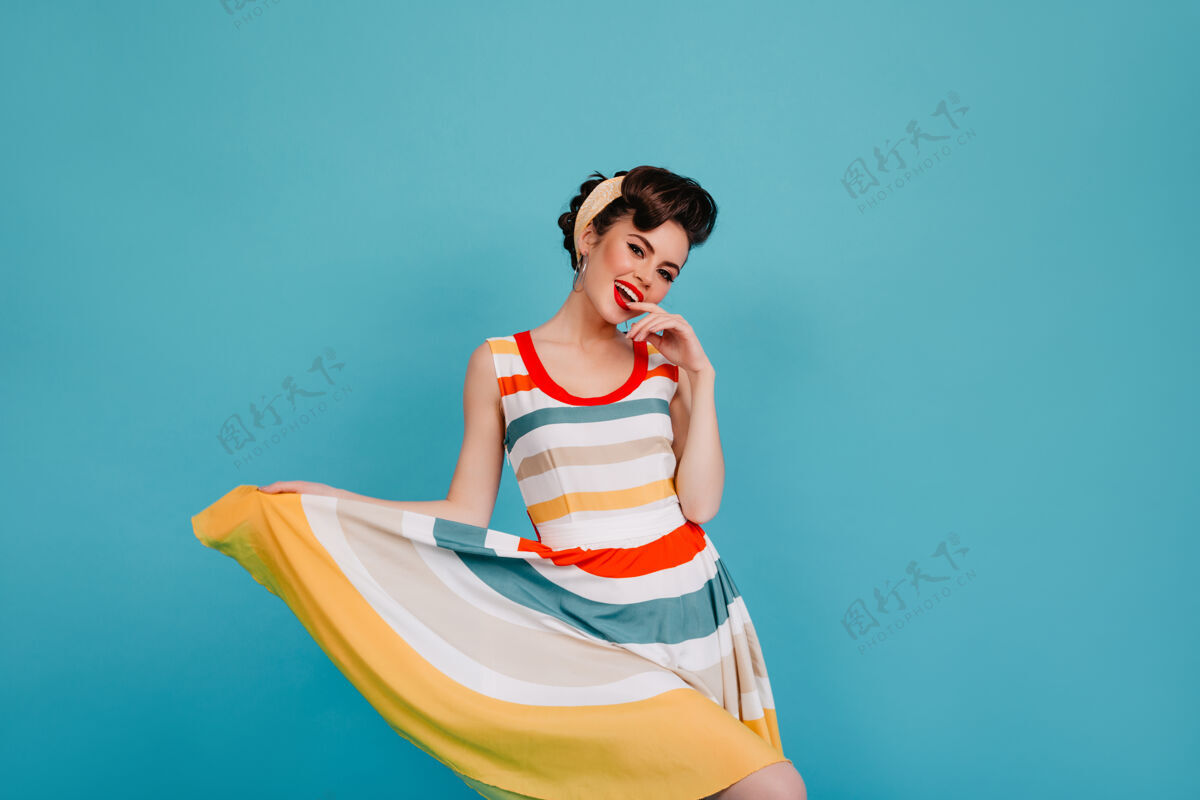 性感兴奋的小女孩玩着条纹连衣裙在蓝色背景上跳舞的笑女人的摄影棚镜头女孩深色优雅