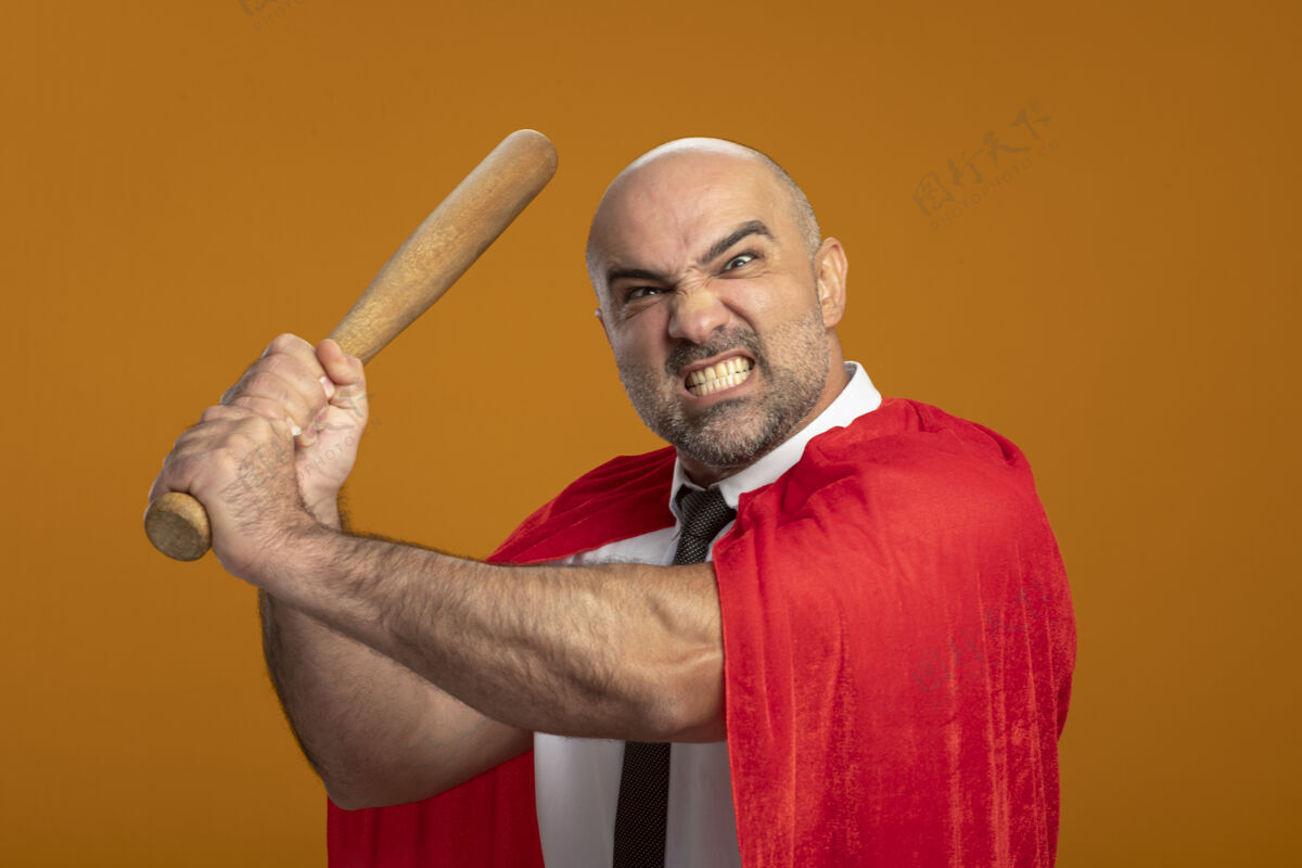 商人穿着红色斗篷的超级英雄商人站在橘色的墙上挥舞着棒球棒 带着愤怒的侵略性表情 发狂橙色超级英雄工作