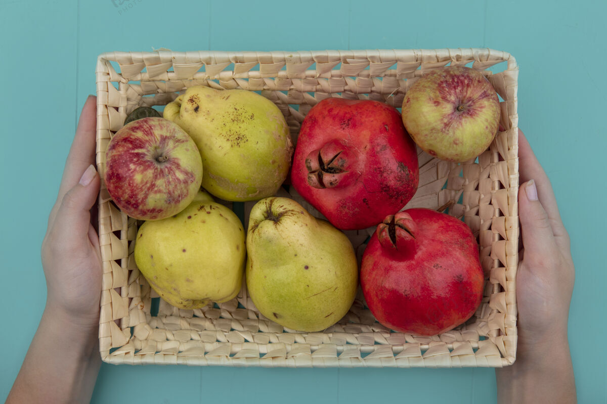 新鲜女性手拿着一桶新鲜水果的俯视图 比如苹果 石榴和木瓜 背景是蓝色的水果食物视图