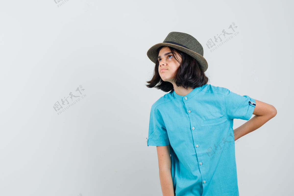 优雅穿蓝衬衫的年轻女士 戴着帽子 手放在脊柱上 看起来很不安时尚女性麻烦