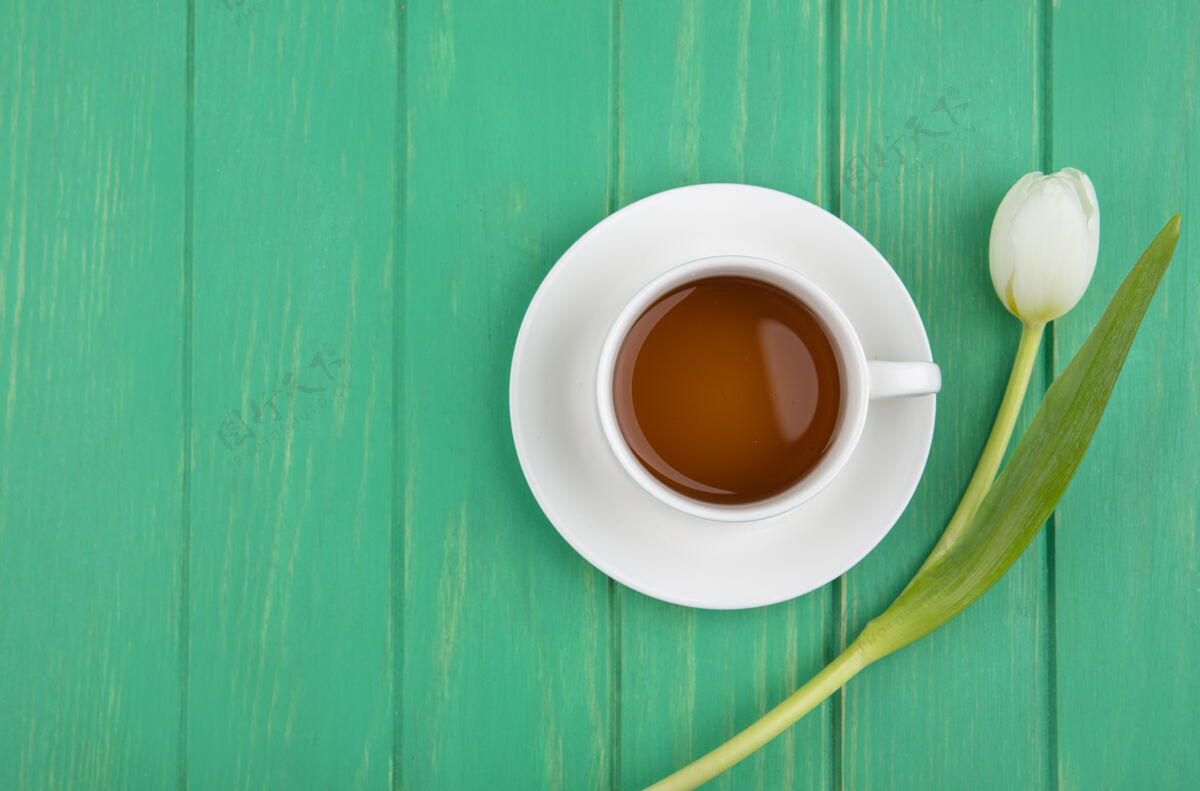 复制茶碟上的茶杯和绿色背景上的花朵顶视图 带有复制空间茶碟绿色饮料