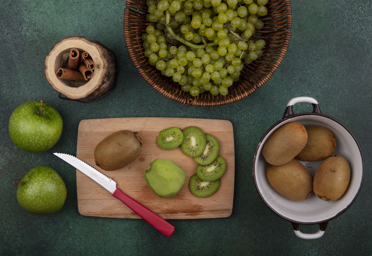 新鲜顶视图猕猴桃在平底锅与切片和刀架上与苹果和葡萄肉桂绿色背景支架刀多汁