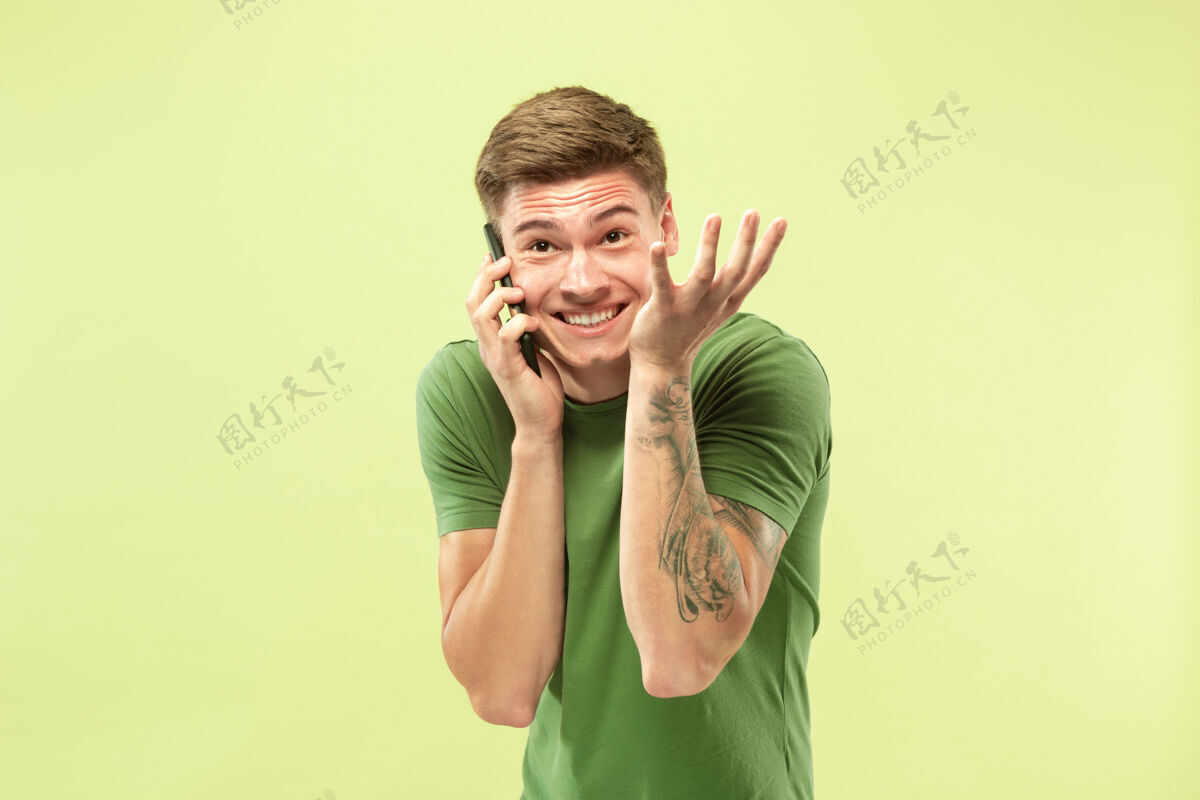 人绿色工作室背景上的白人年轻人半身肖像穿着衬衫的漂亮男模人类情感的概念 面部表情 销售 广告打电话 看起来很开心手势年轻男性