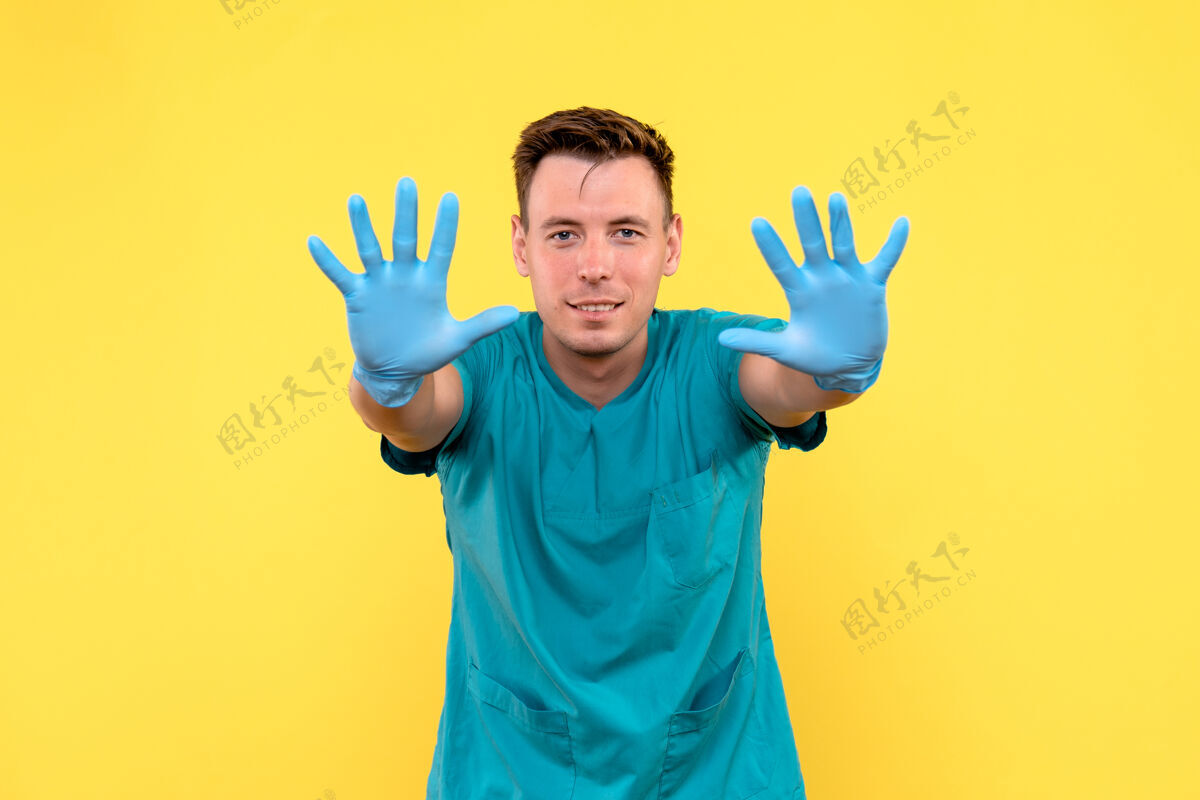 青年黄墙上戴着蓝手套的男医生的正视图手医疗男人