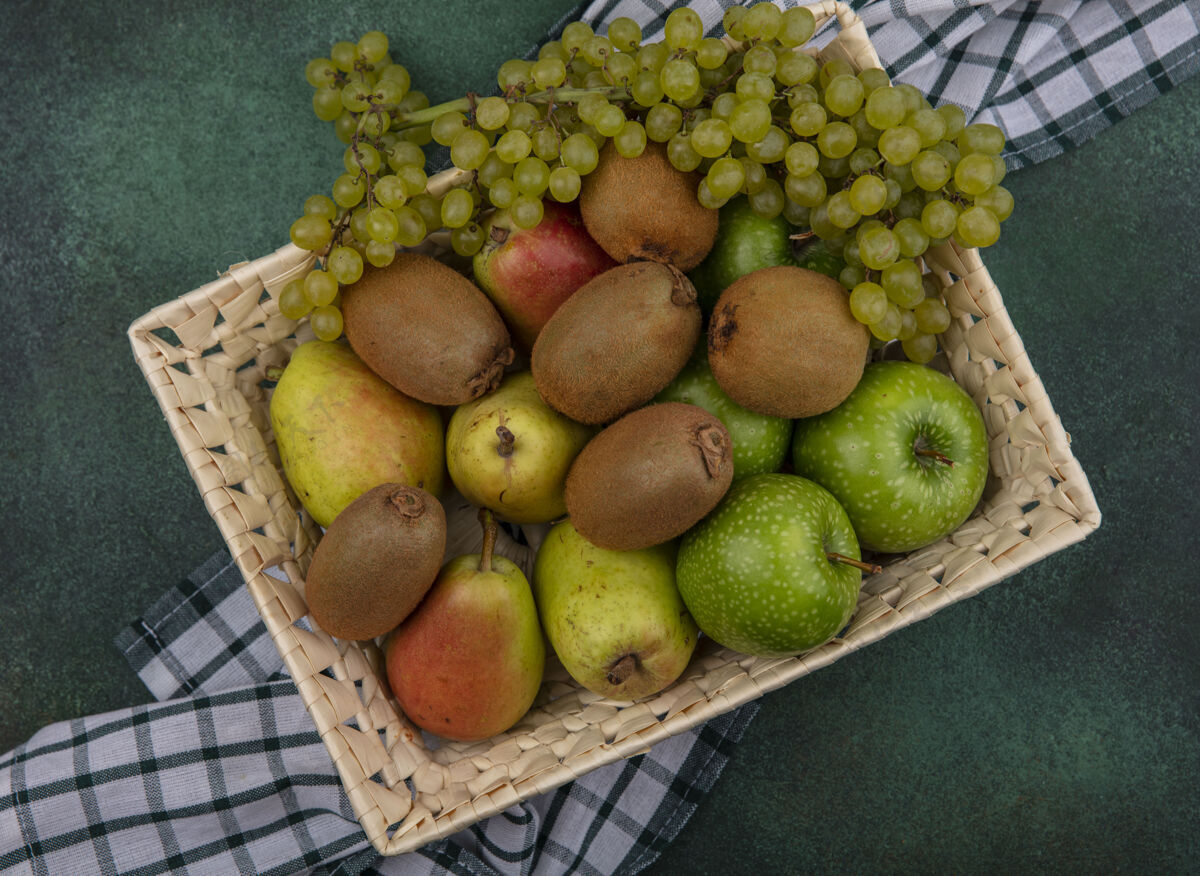 新鲜在绿色的背景下 在格子毛巾上的篮子里放着绿色的苹果 葡萄和梨葡萄水果猕猴桃