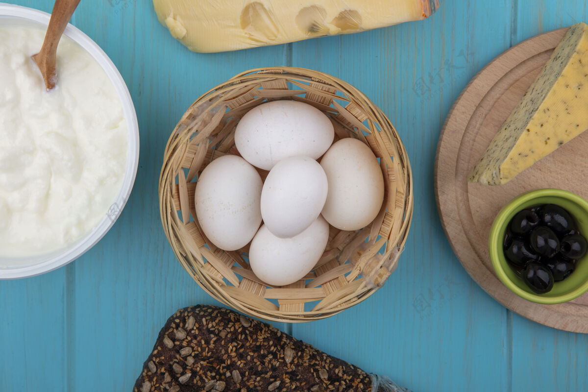 篮子顶视图鸡蛋在一篮子奶酪与黑面包和酸奶在一个碗在一个绿松石背景食物鸡蛋黑面包