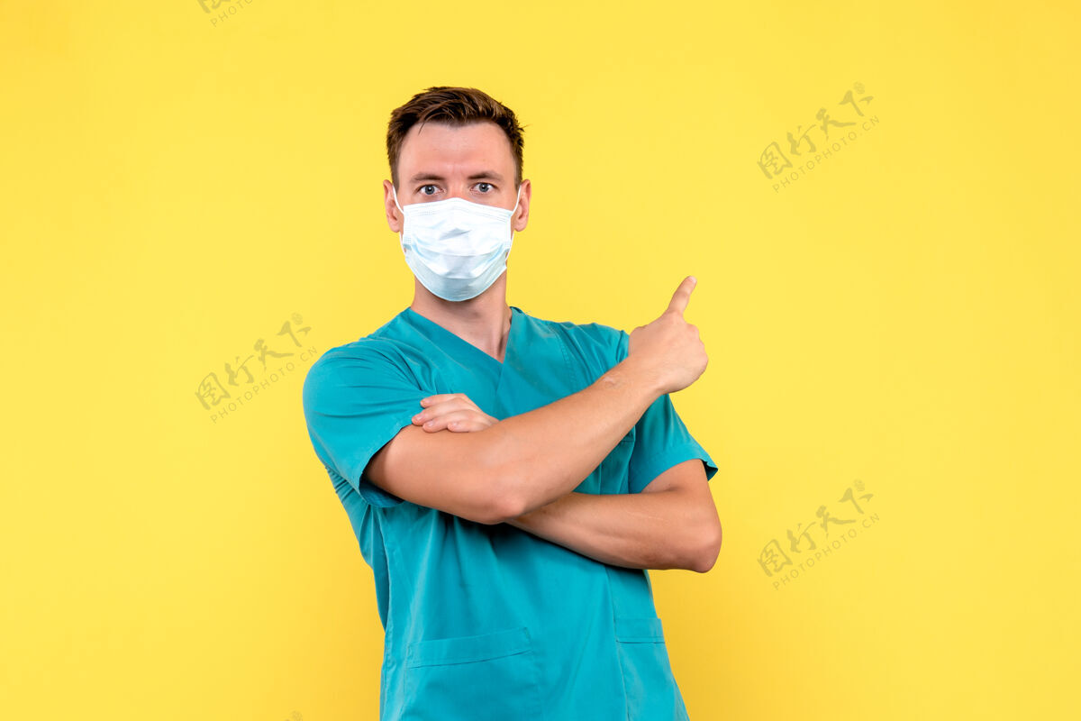 正面黄色墙上戴着无菌口罩的男医生的正视图人帅哥绝育