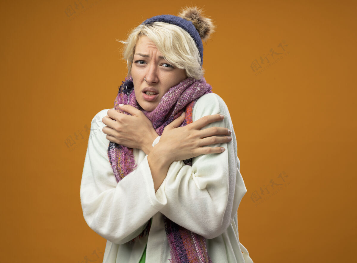 女人生病的不健康的女人 短发 戴着暖和的围巾和帽子 发烧 站在橙色的墙上感觉不舒服生病痛苦暖和
