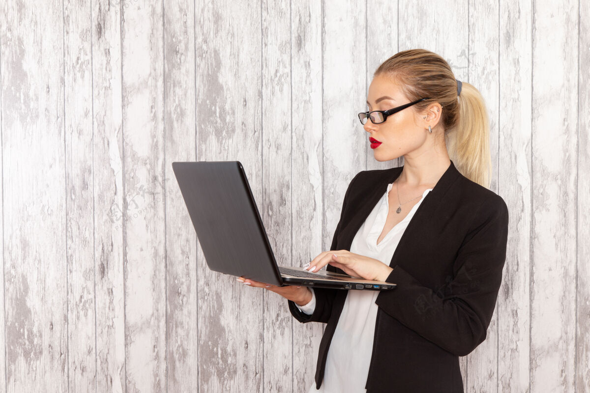 执行正面图穿着严苛衣服的年轻女商人黑夹克在白墙上用笔记本电脑办公前面笔记本电脑工作