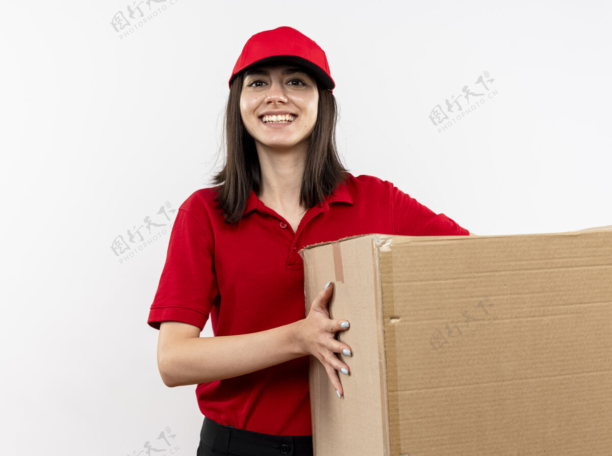 站着年轻的送货员身穿红色制服 戴着帽子 手里拿着大纸盒 脸上带着微笑站在白色的墙上盒子帽子女孩