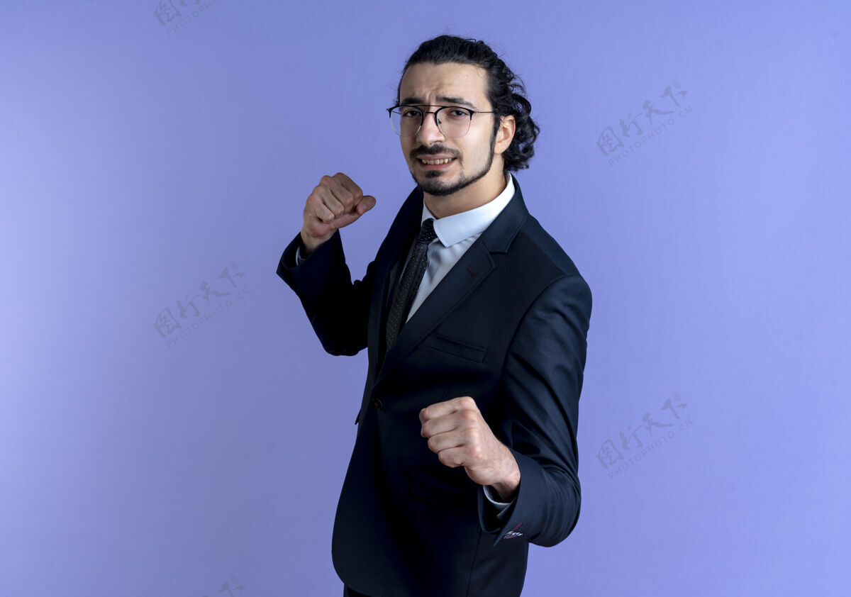 家伙一个穿着黑色西装戴着眼镜的商人望着前面紧握的拳头 像一个拳击手站在蓝色的墙上公民人喜欢
