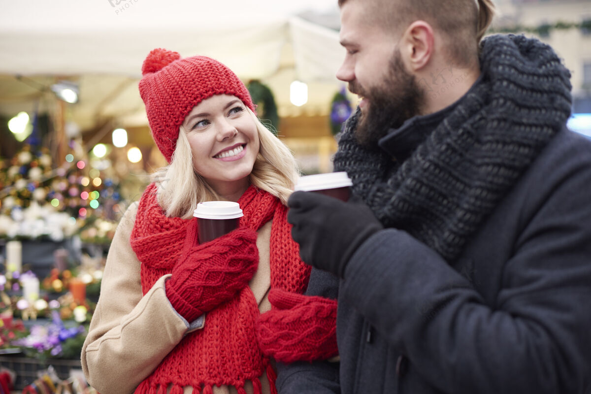 牙齿微笑在圣诞集市上喝咖啡的情侣户外面对面冬天
