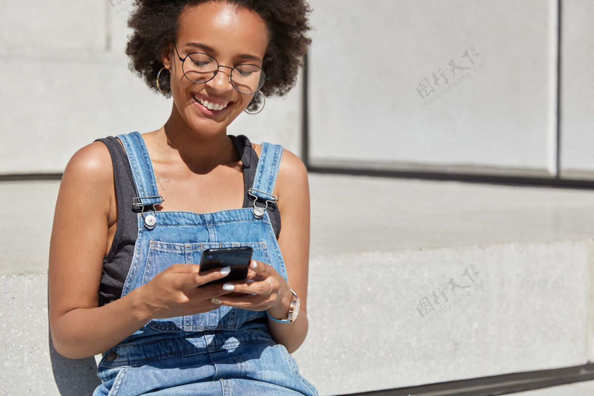 打字人 娱乐和科技的概念轻松无忧无虑的黑人妇女手里拿着手机 给朋友打短信 有愉快的表情 为您的文字信息腾出空间非洲消遣电话
