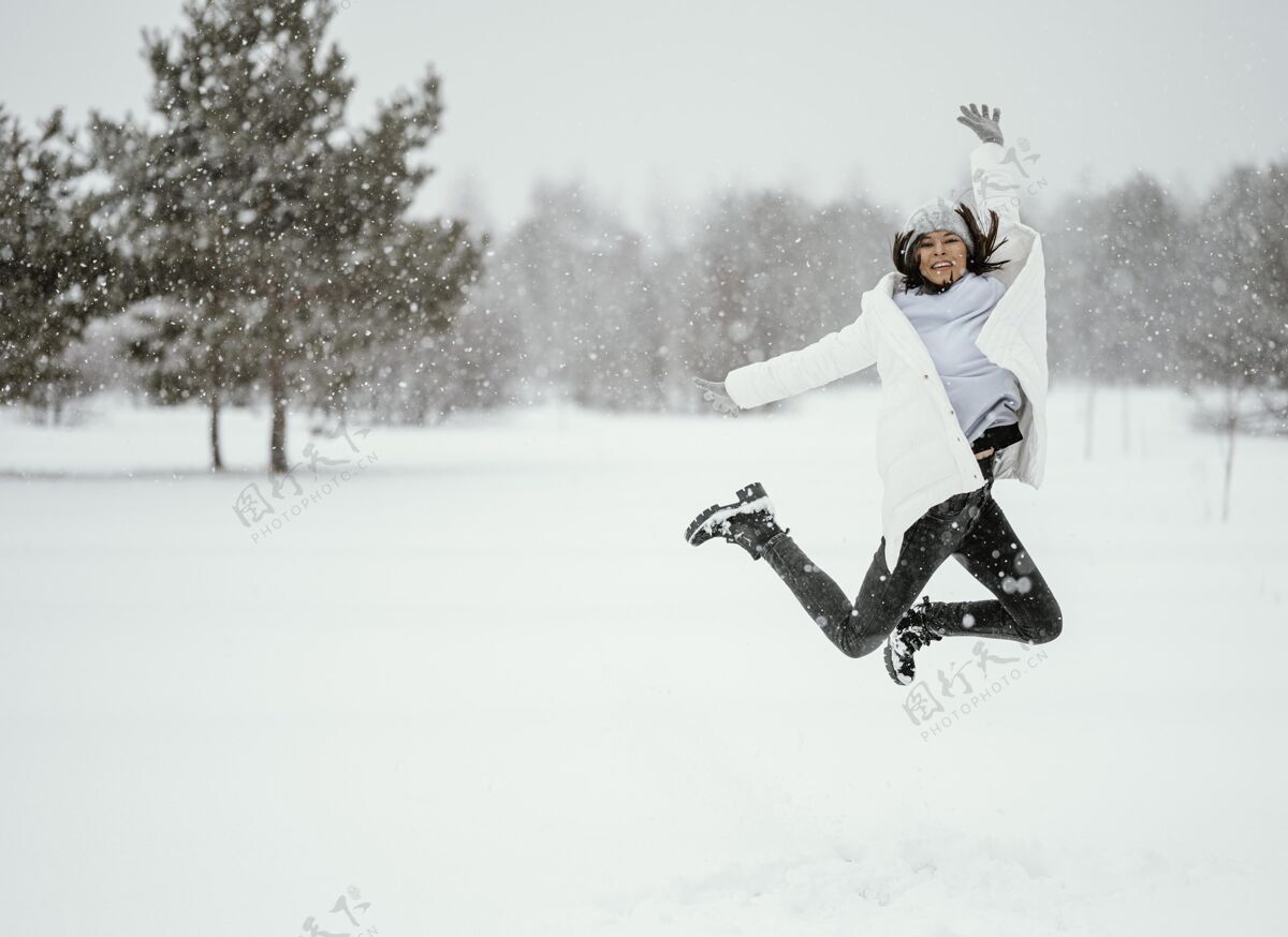 个人冬季在户外空中跳跃的女人的正面图雪户外姿势