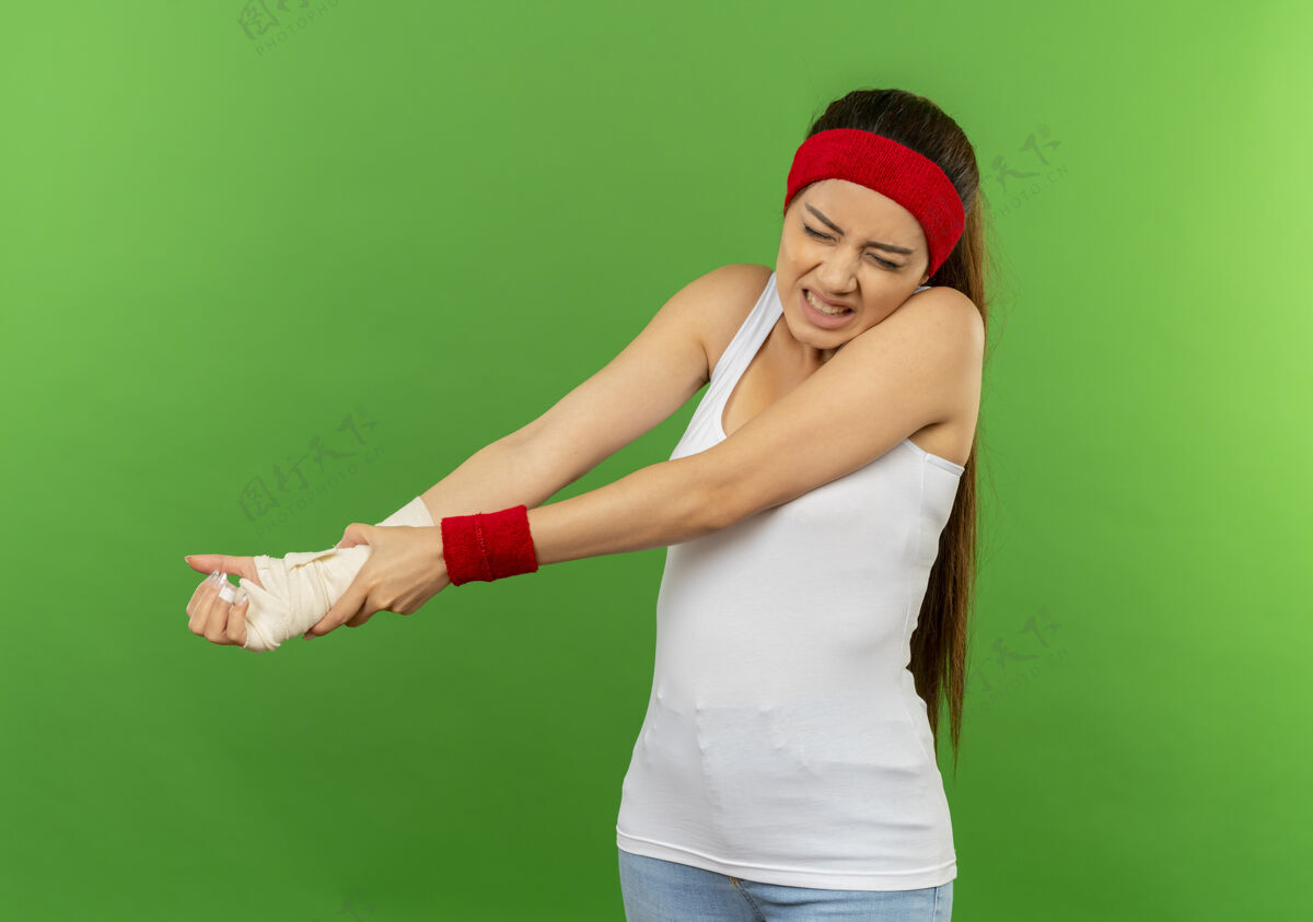 不适一位身穿运动服 头箍贴着绷带的年轻健身女士站在绿色的墙上 看起来很不舒服绷带头带运动