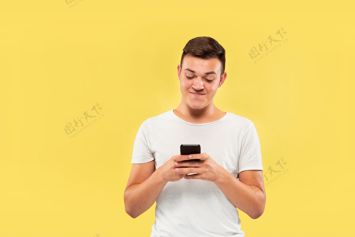 成功黄色工作室背景上的白人年轻人半身肖像穿着衬衫的漂亮男模人类情感的概念 面部表情 销售 广告使用电话 看起来疯狂快乐工作表情公司