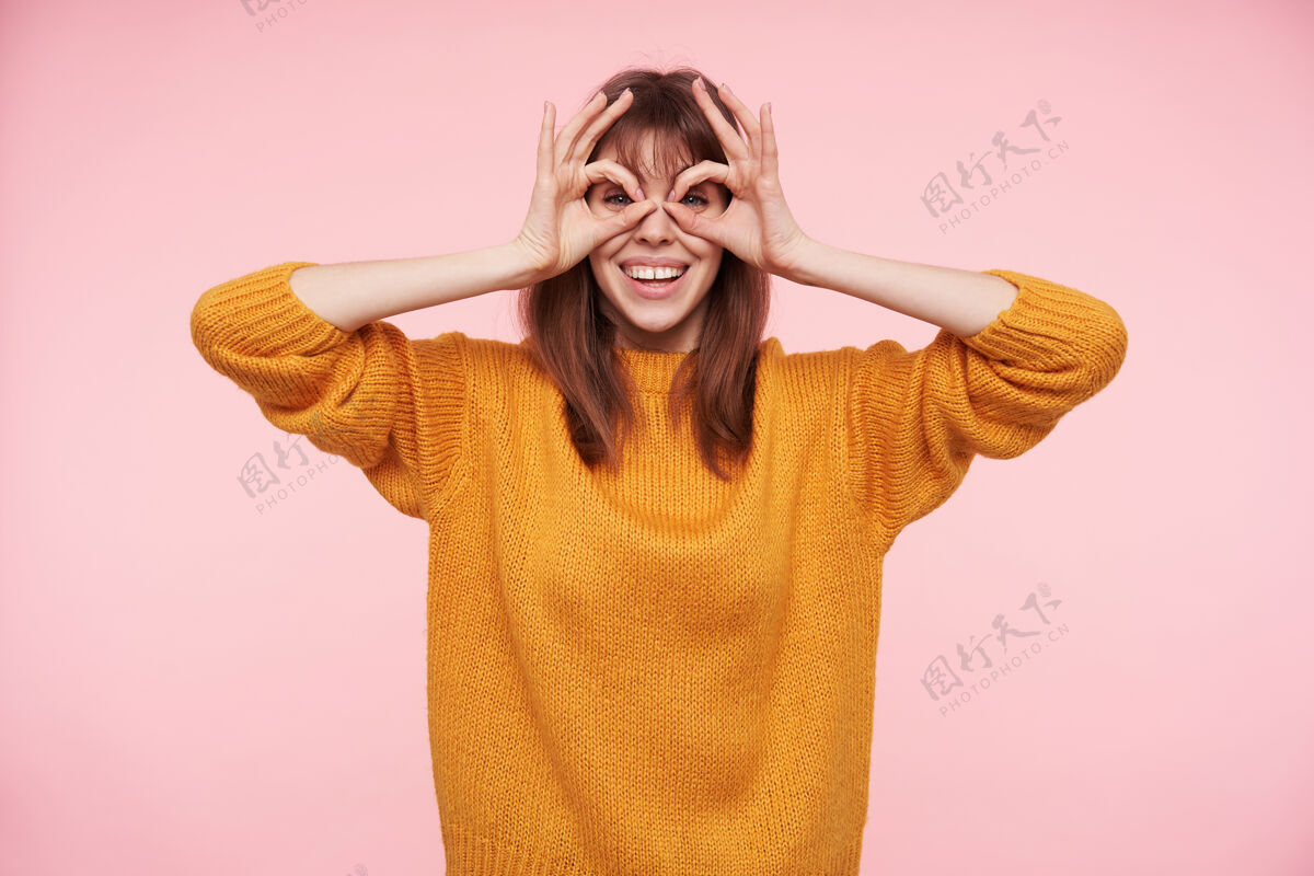 前锁年轻快乐的黑发女子 穿着休闲服 站在粉红色的墙上 举手微笑 脸上露出喜色爱表情积极
