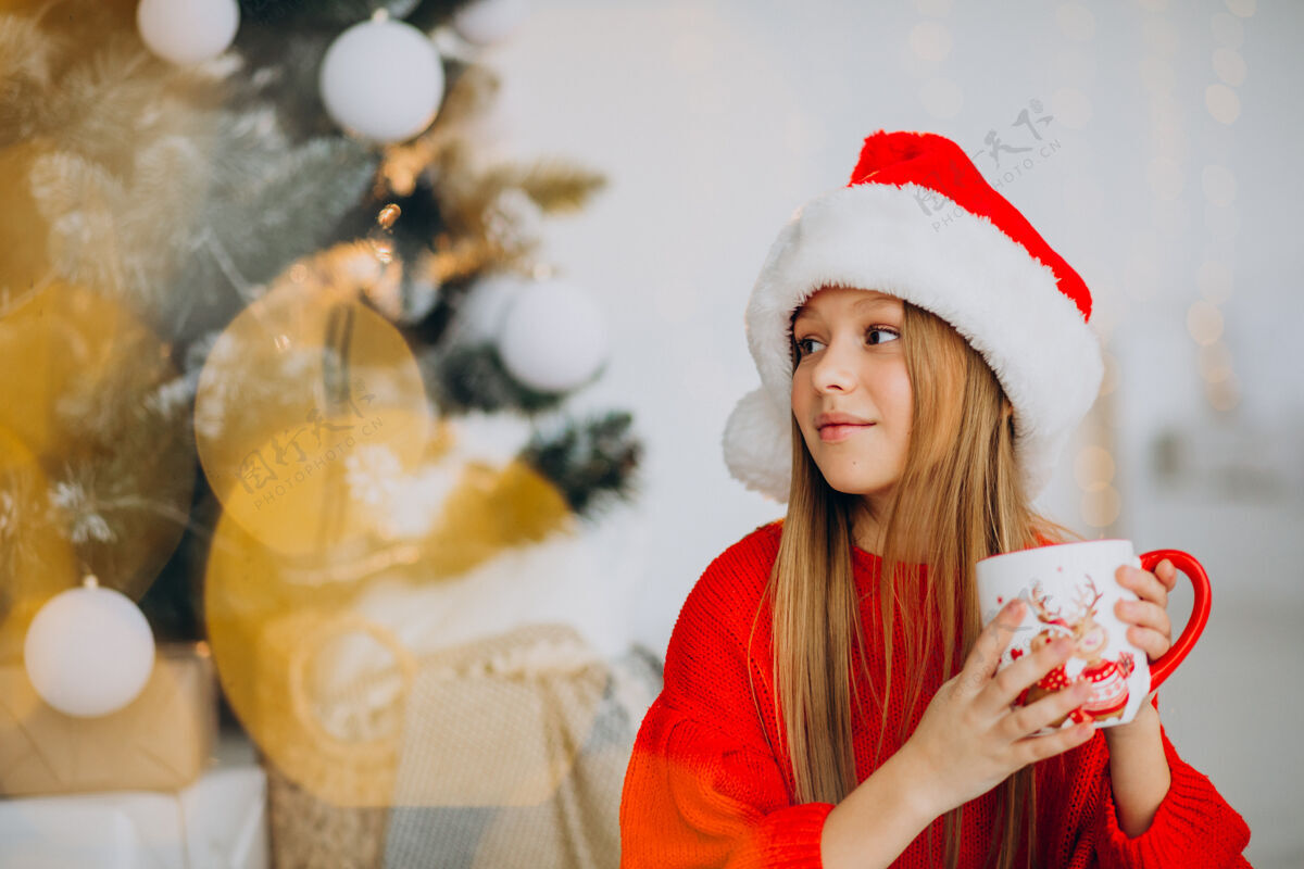 庆祝在圣诞树旁喝可可的女孩乐趣年轻圣诞树