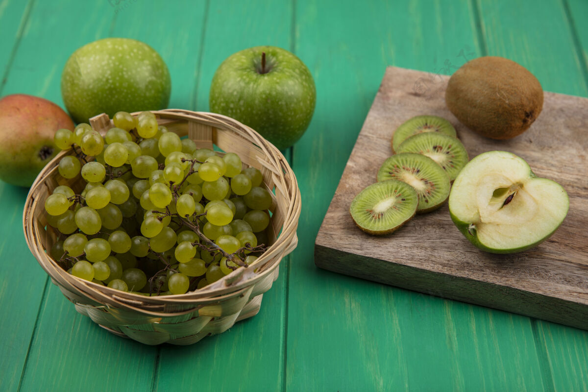 苹果侧视图猕猴桃片上的立场与绿色的苹果和梨与绿色的葡萄在一个篮子在绿色的背景猕猴桃架子葡萄