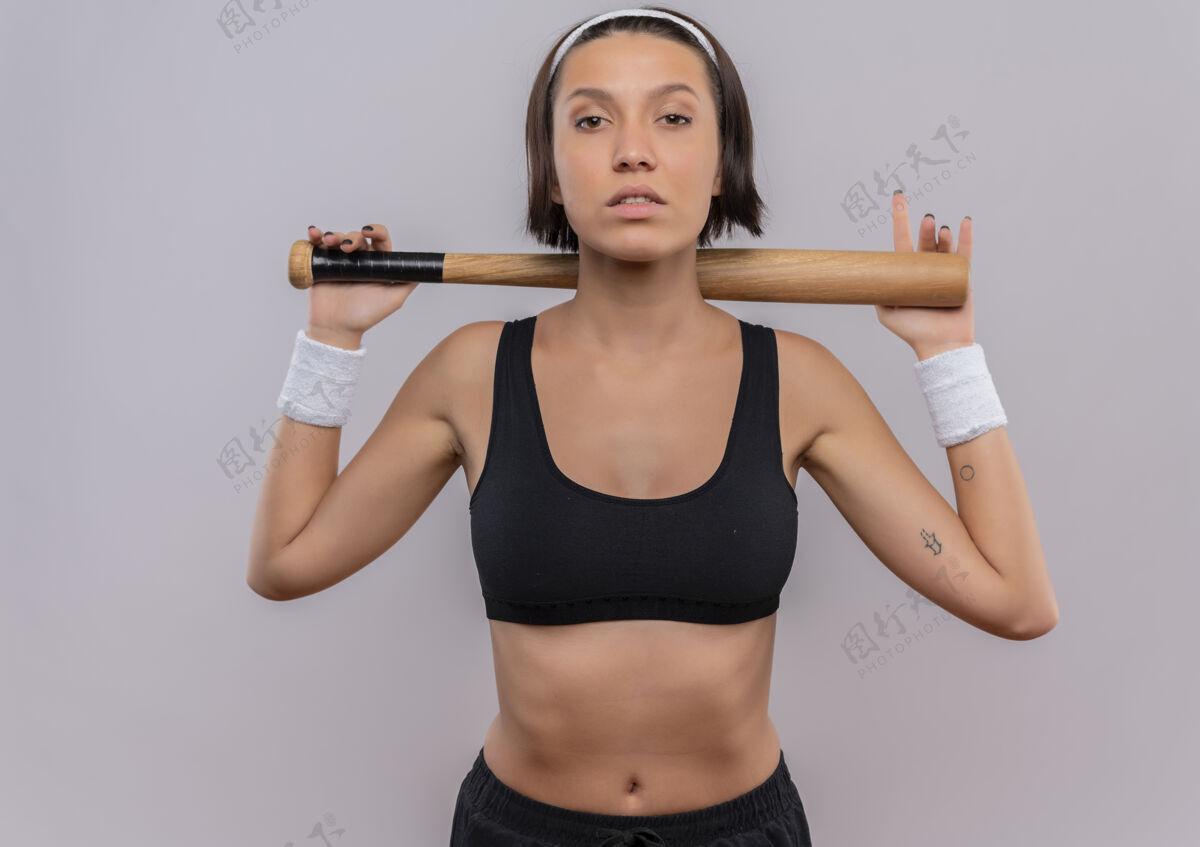 运动身穿运动服 手持棒球棒 微笑自信地站在白墙上的年轻健身女士健身自信年轻人