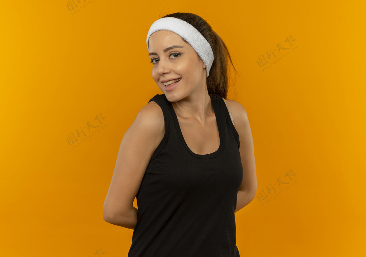 运动胆小的年轻健身女 戴着运动服 脸上挂着微笑 站在橙色的墙上运动装摆姿势微笑