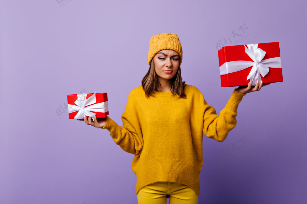 爱有趣的黑发女士 戴着时髦的帽子 手里拿着礼物盒圣诞前穿着黄色毛衣的迷人黑发女士的肖像休闲放松欢呼