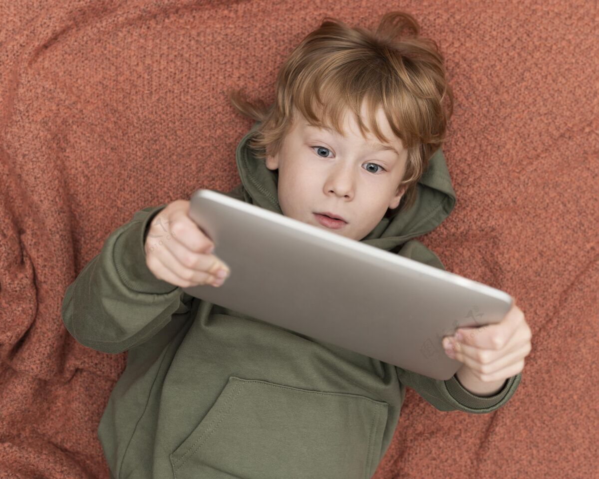 平板电脑小男孩在床上使用平板电脑的俯视图设备娱乐男孩