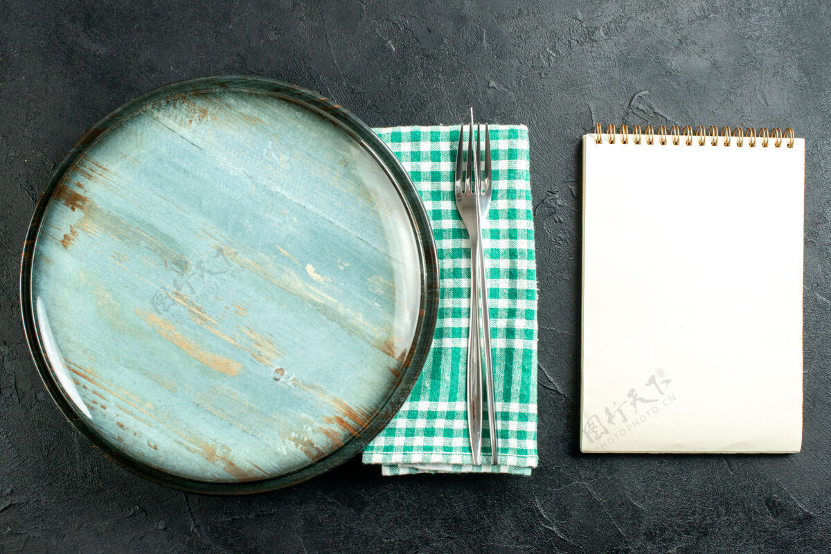 笔记本俯视图圆形拼盘餐刀和叉子在绿色和白色方格餐巾笔记本在黑色的桌子上餐巾纸培养皿晚餐