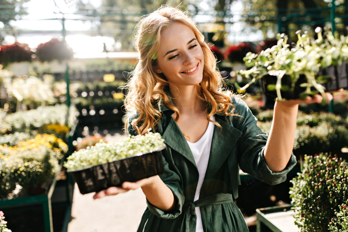 表情一位金发碧眼 笑容温柔的年轻女子 身着绿色长袍 系着腰带 正在温室里工作脸植物温室