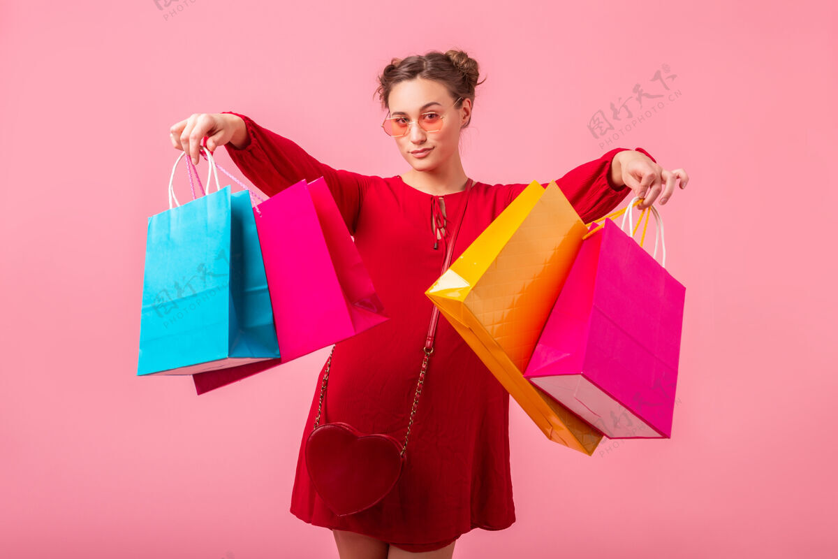 包迷人快乐搞笑情感时尚女性购物狂身着红色新潮连衣裙手捧五颜六色购物袋在粉色墙壁上孤零零出售 销售兴奋 春夏时尚潮流乐趣肖像购物