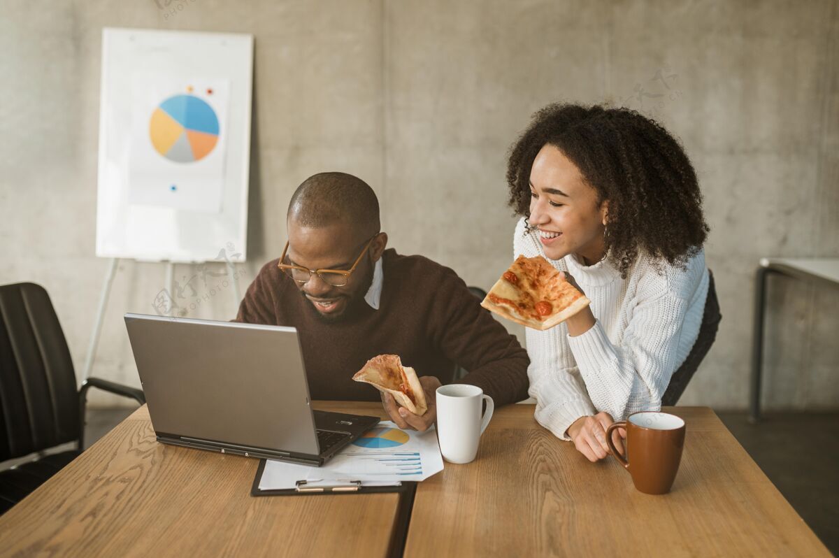 咖啡两个笑眯眯的同事在办公室会议休息时吃比萨饼披萨公司笔记本电脑