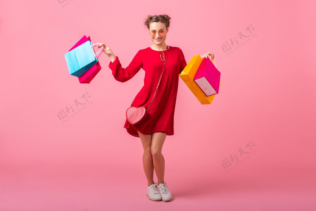 白天迷人快乐微笑的时尚女性购物狂身着红色新潮连衣裙手持五颜六色的购物袋贴在粉色的墙上 销售兴奋 春夏时尚潮流衣服身高商店