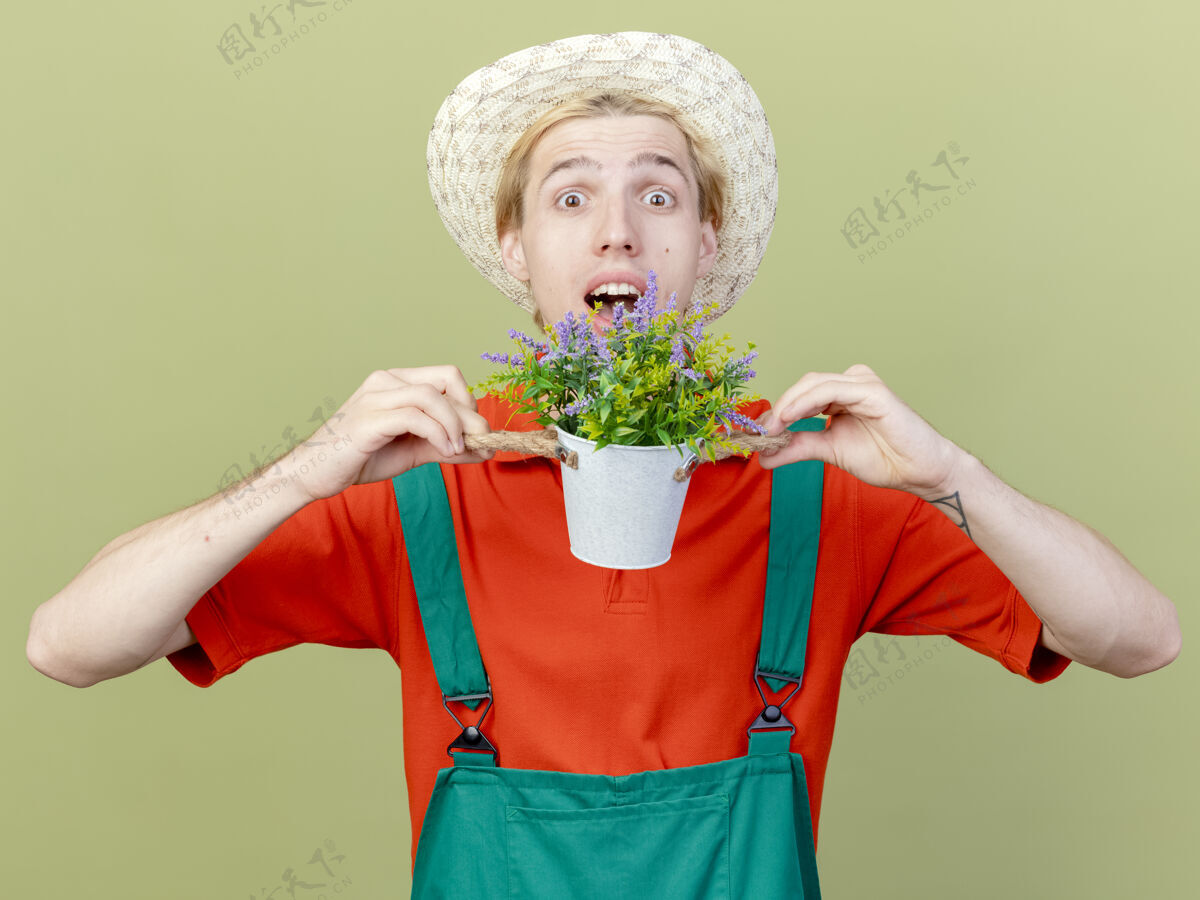 站年轻的园丁穿着连体衣戴着帽子拿着盆栽植物花园帽子抱