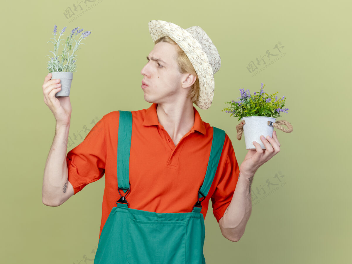 光年轻的园丁 穿着连体衣 戴着帽子 手里拿着盆栽植物帽子穿连身衣