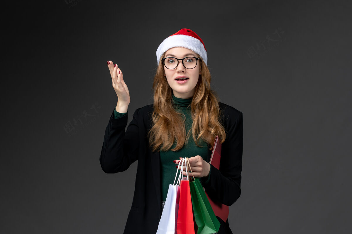 年轻女性正面图：年轻女性带着黑色墙壁上的包装礼物新年礼物节日成人漂亮圣诞节