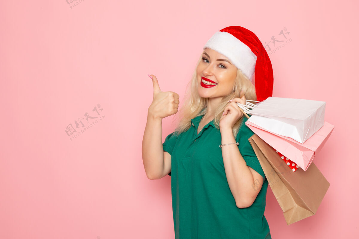 肖像正面图：年轻女性手拿圣诞礼物 在粉红色的墙上微笑 圣诞节照片模特新年假期美丽包装年轻女性