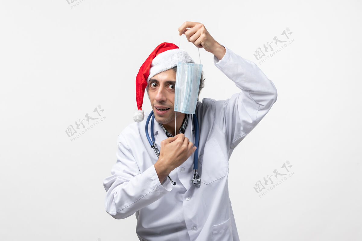 视图正面图男医生拿着口罩在白墙上共舞新年假期病毒球员制服病毒