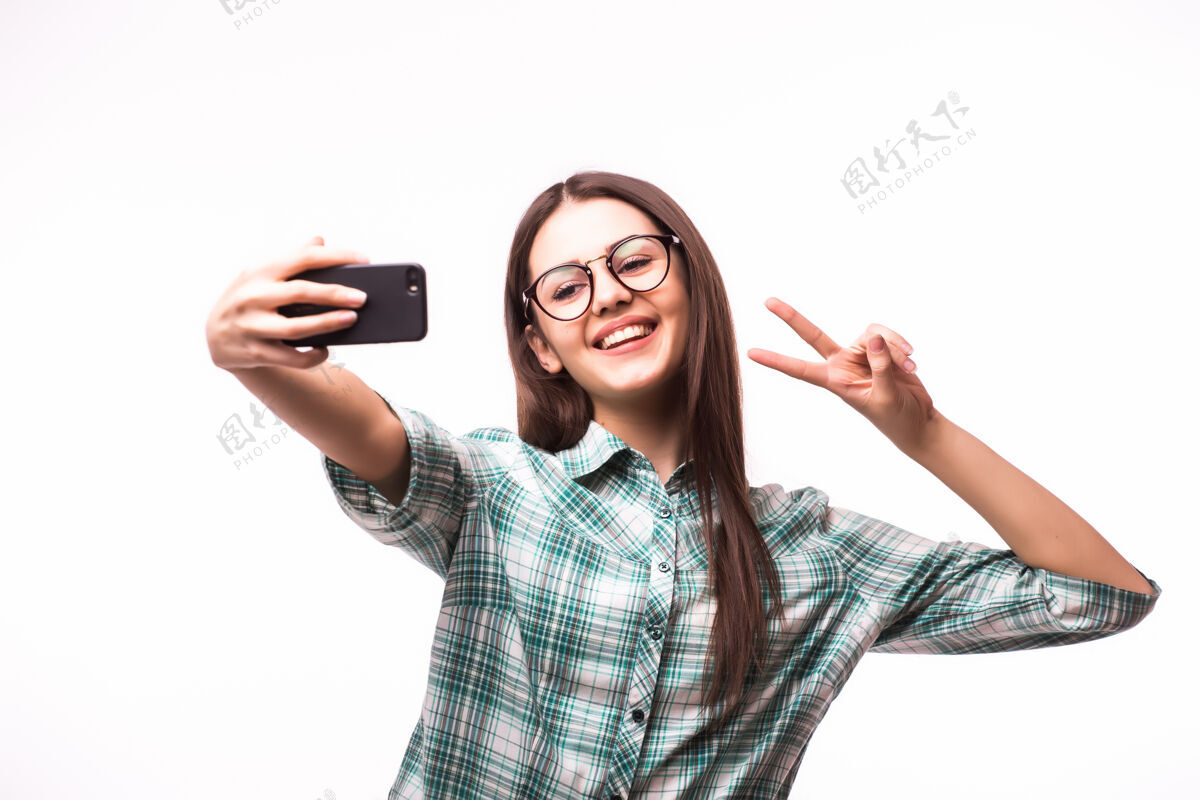 手美丽的年轻女子手持手机和自己的照片 而站在白色的手机自拍年轻