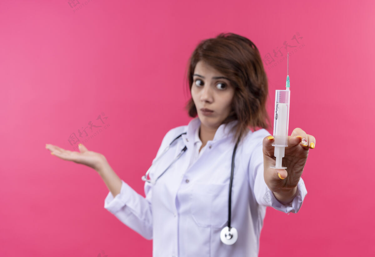 医生穿着白大褂的年轻女医生拿着听诊器 手里拿着注射器 神色迷茫 不确定地将手臂伸向一边侧身注射器听诊器