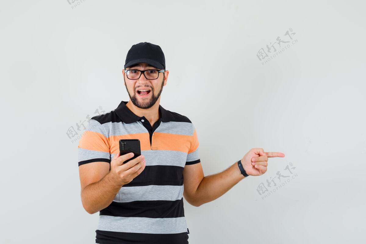 手机年轻人手里拿着手机 指着旁边的t恤 戴着帽子 表情积极 正面看去成功肖像休闲