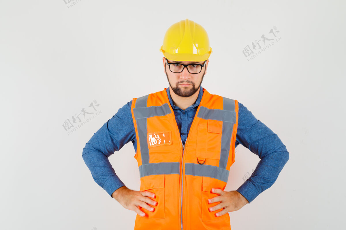 背心年轻的建设者手挽腰 穿着衬衫 背心 头盔 表情严肃正面图杂工建筑年轻