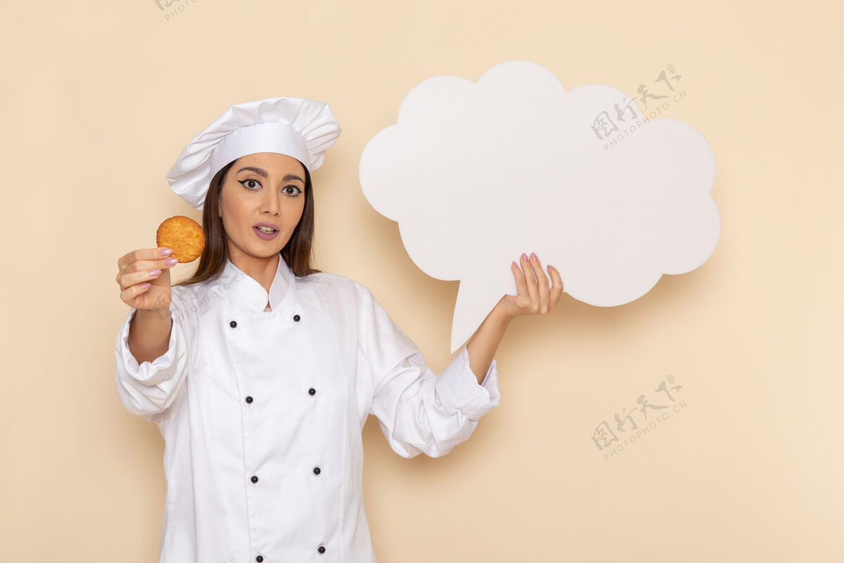 套装身穿白色厨师服的年轻女厨师的正面图 在浅白的墙上举着白色的牌子脸烹饪手持