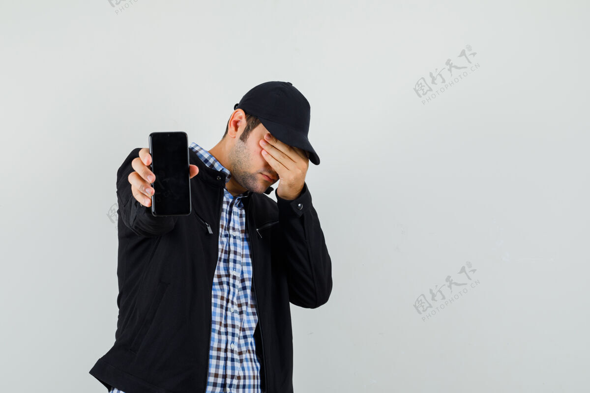 男年轻人拿着手机 手放在衬衫 夹克 帽子 前视图的眼睛上自信朋友站