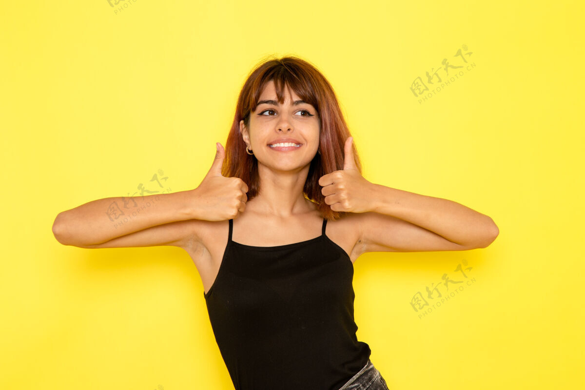 漂亮身穿黑色衬衫和灰色牛仔裤的年轻女性在黄色墙壁上微笑的正面视图衬衫粉碎性感